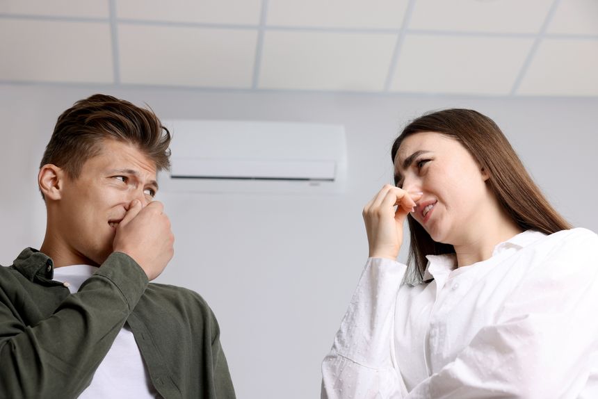 Unhappy couple suffering from bad smell and covering their noses near air conditioner indoors, low angle view