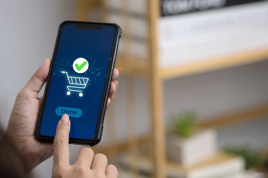 Woman confirming online shopping order via smartphone app with shopping cart and green check mark icon on screen.