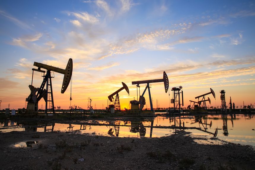 Oil field site, in the evening, oil pumps are running, The oil pump and the beautiful sunset reflected in the water, the silhouette of the beam pumping unit in the evening.