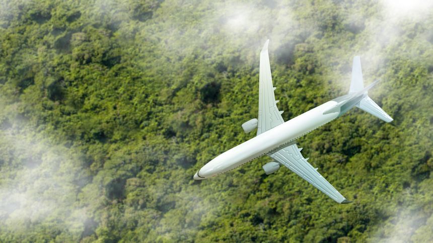 Aerial view of an airplane flying over the clouds with a lush tropical landscape. Concept of travel