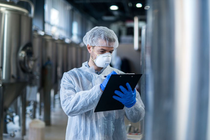 Technologist specialist keeping track of production process and writing notes in his logbook. Responsible young man at his workplace.