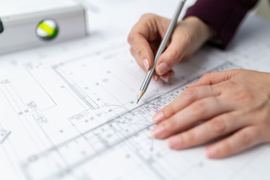 A person measures and marks an architectural drawing with a pencil and clear ruler over a printed building plan.
