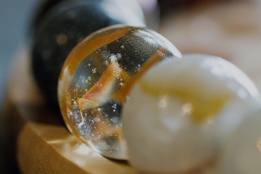 A close up macro photo of colorful glass marbles on a wooden tray. Sunlight is shining through and reflecting off of the marbles.