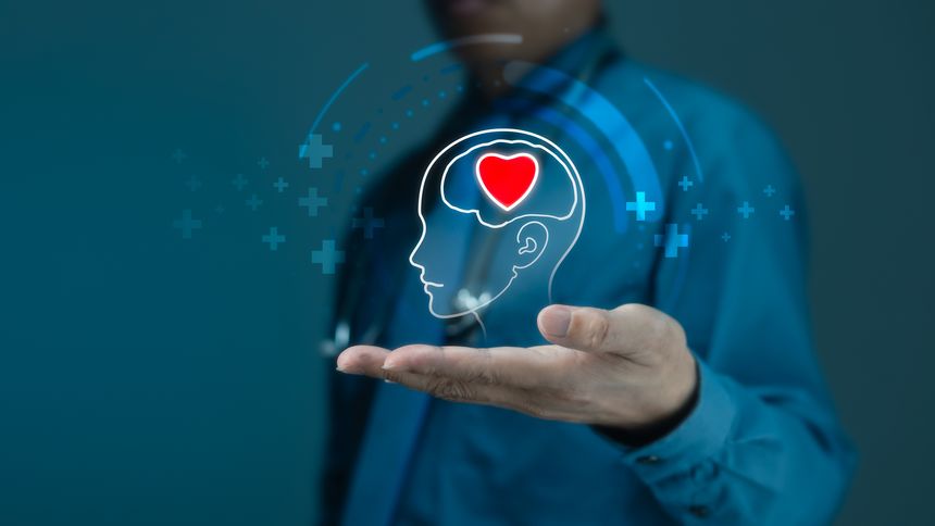 Doctor's open hand supports a glowing holographic outline of a human head with a vibrant red heart inside, symbolizing mental health and emotional well-being