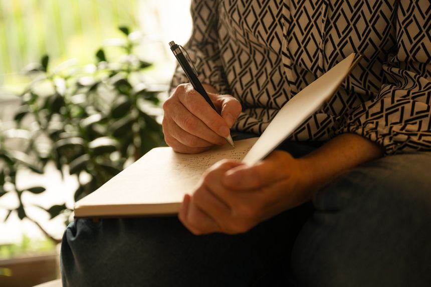 Middle-aged woman writing notes in notebook while sitting at home, reflective and productive evening scene, selective focus