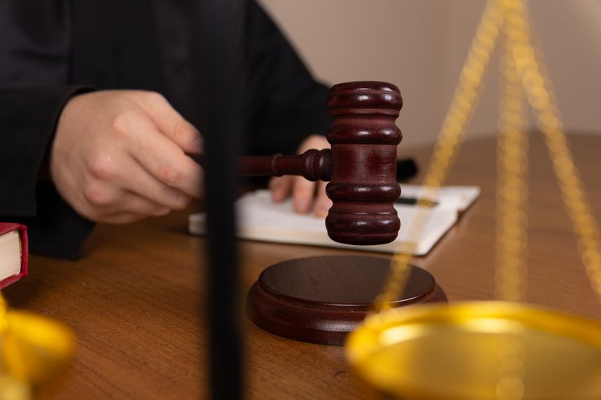Judge holding a gavel on wooden table in courtroom.