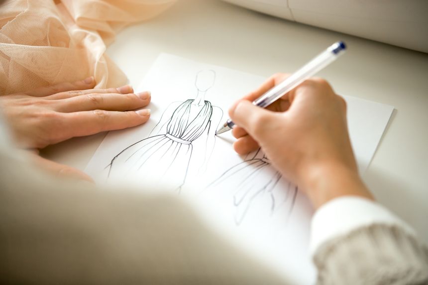 Hands drawing a black ink clothing design sketch, view over the shoulder, closeup, close-up