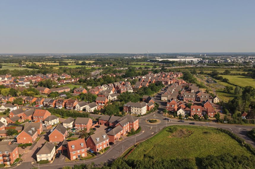 Aerial drone footage of Three Mile Cross in Berkshire, England, showcasing residential neighbourhoods, surrounding countryside, and suburban development. Elevated view highlighting the blend of modern housing and green landscapes in southern England.