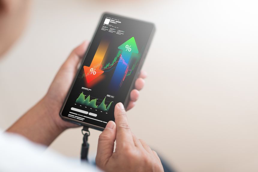 A close-up shot shows a person's hand holding a smartphone, displaying a complex financial analysis interface with upward and downward trending percentage arrows, stock market charts, and various data points. This image is perfect for illustrating concepts like investment, trading, financial growth, economic analysis, and mobile financial management.