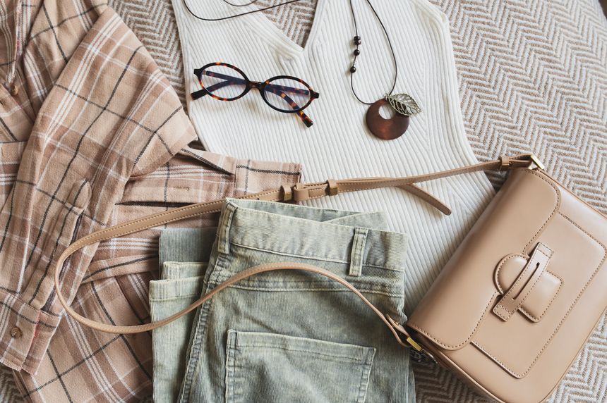 flat lay of woman spring fashion collection in casual style. Top view of plaid shirt, handbag, jeans and top in light beige tones