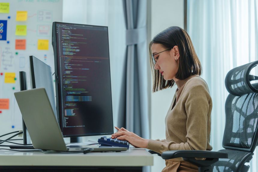 Asian prompt engineer develop coding app with software data sitting in front of computer monitor at office
