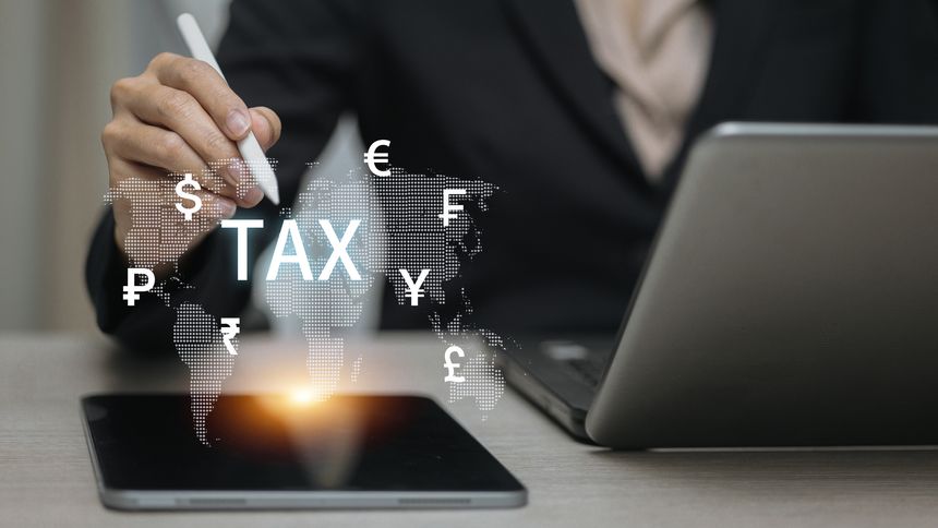 Businessman using tablet with stylus showing TAX icon and global currency symbols, digital tax system, online finance, and international economy concept.