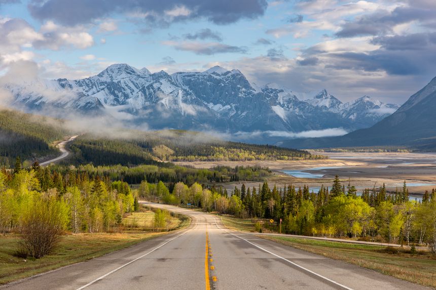 Mountain highway descending toward dramatic Rocky Mountain valley. Fast flowing turquoise mountain river, canyon rock formations and evergreen forest in the Canadian Rockies, Alberta, Canada.