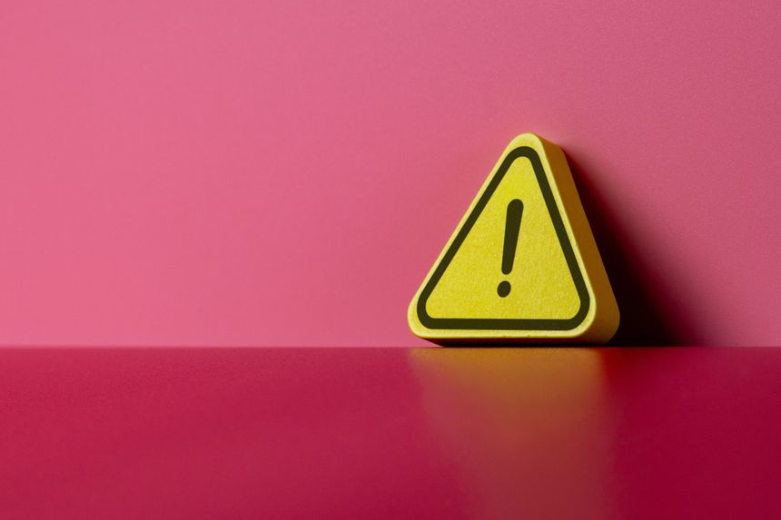 A yellow warning triangle with a black exclamation mark leaning against a pink wall. Caution, error, alerts, hazards, and attention concept. Copy space for text.