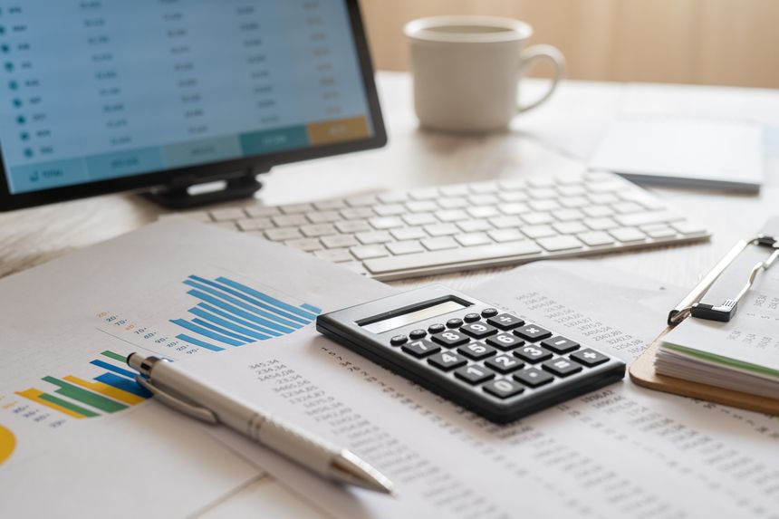 Financial manager reviewing budgeting data and accounting reports with a calculator, pen, and tablet on a business desk, analyzing corporate performance and planning future investments