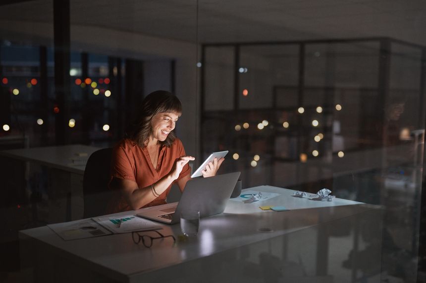Shot of a young businesswoman working on a digital tablet and laptop in an office at night